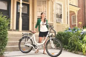 Woman with an electric bicycle in front of a suburban home, suggesting eco-friendly lifestyle and urban commuting.